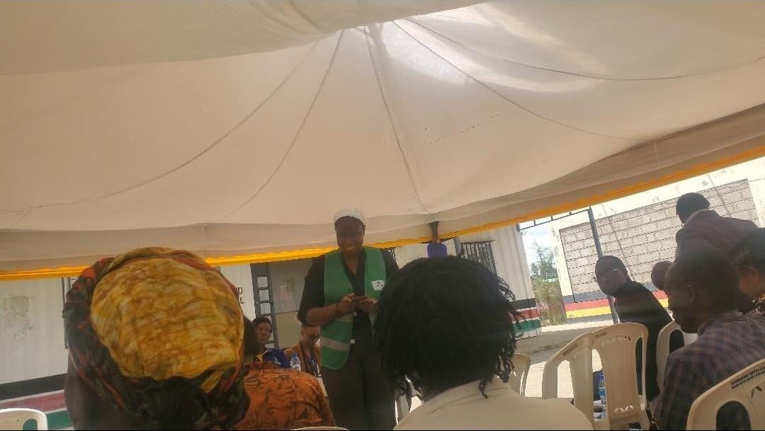 A CRE-CBO team member facilitating a community meeting under a tent